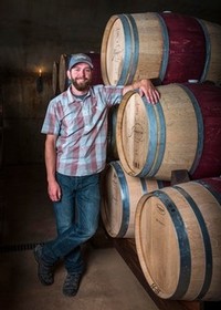 Winemaker, Bradley Long, leans on a stack of wine barrels